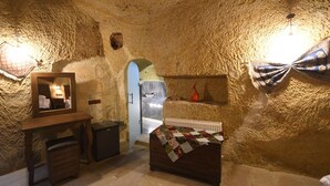 A rustic stone room with a bed, dresser, mirror, and a small kitchenette. - Rose Nest Cave Otel (Ürgüp)