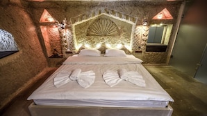 A stone-walled room with a bed, two wall-mounted lights, and a stone bench. - Rose Nest Cave Otel (Ürgüp)