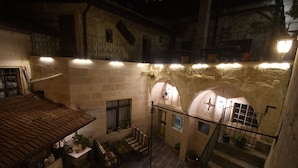 A stone courtyard with a tiled roof, a staircase, and a small seating area with cushions and a table. - Rose Nest Cave Otel (Ürgüp)