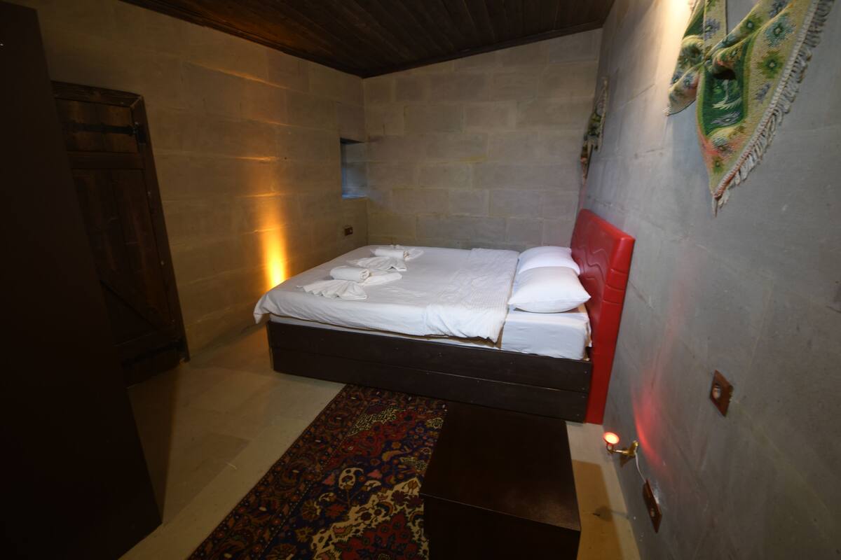 Quarto com cama, porta de madeira, tapete estampado e luminária fixada na parede.