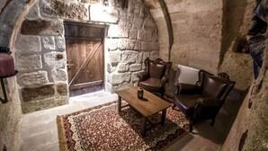 A cozy room with stone walls, a wooden door, a patterned rug, a wooden table, and two leather armchairs. - Rose Nest Cave Otel (Ürgüp)