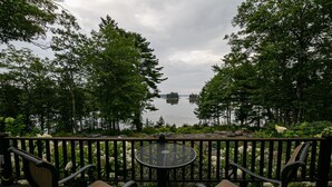 Una terraza con dos sillas y una mesa, con vista a un lago rodeado de árboles.