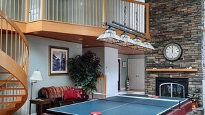 Un salón amplio con mesa de billar, una escalera, chimenea y un reloj en la pared.