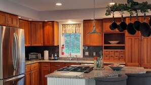 Una cocina moderna con armarios de madera, electrodomésticos de acero inoxidable, una isla central con taburetes altos y utensilios colgantes.