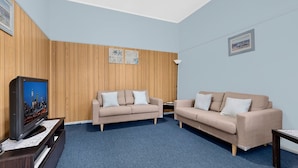 A room with two beige sofas, a television, and wooden panel walls. - Hutton Hide Away - East Coast Getaways (The Entrance North)