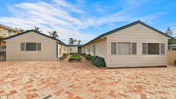 A row of two-story buildings with a brick-paved courtyard, each with a small garden area and a single entrance. - Hutton Hide Away - East Coast Getaways (The Entrance North)