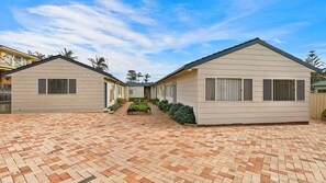 A row of two-story buildings with a brick-paved courtyard, each with a small garden area and a single entrance. - Hutton Hide Away - East Coast Getaways (The Entrance North)