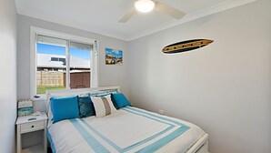 Ein Schlafzimmer mit Bett, Nachttisch, Fenster mit Aussicht und Deckenventilator.