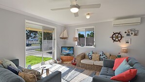 Ein geräumiger Wohnbereich mit großen Schiebetüren zum Garten, einem Deckenventilator, einem Fernseher und einer gemütlichen Sitzecke.