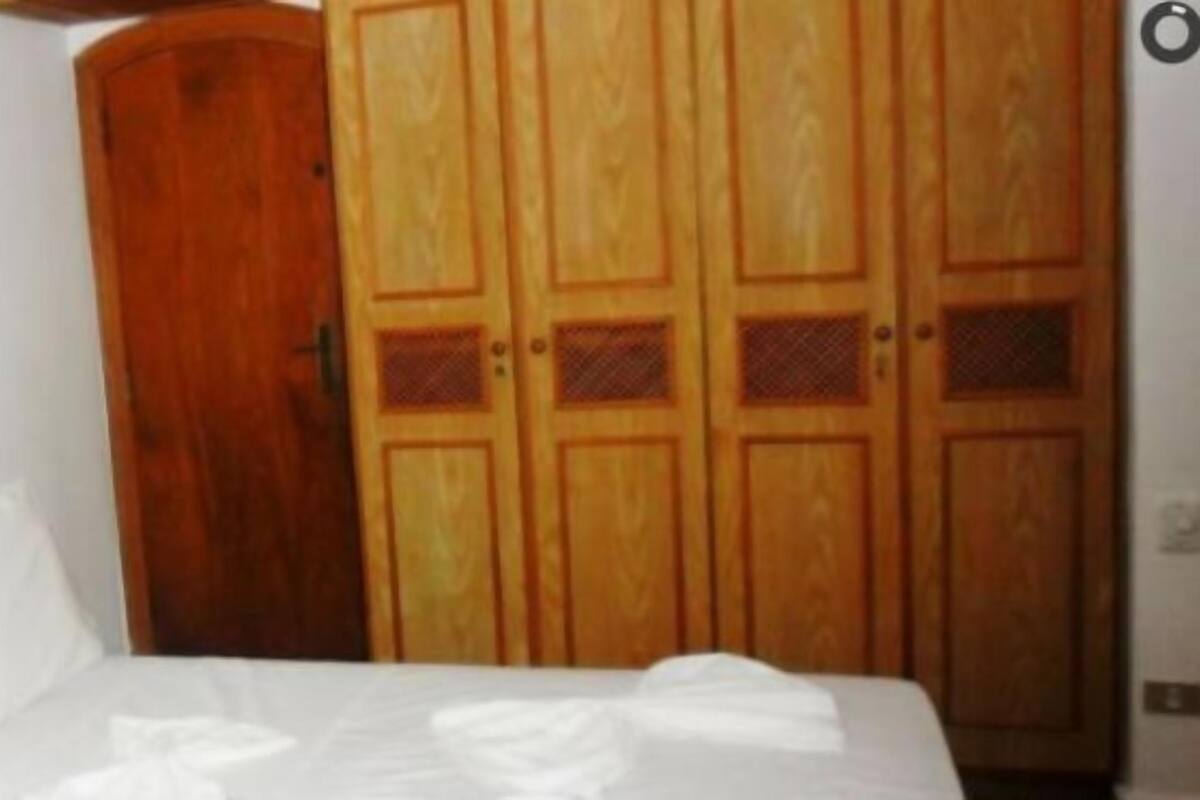 A bedroom with a bed, white pillows, a wooden wardrobe, and a framed picture on the wall.