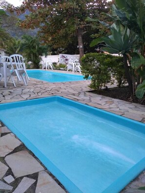 A swimming pool with stone tiles and white plastic chairs around it. - Hotel Portal da Praia (São Sebastião)