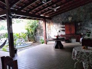 An outdoor patio area with a stone wall, a round table, and a hammock. - Hotel Portal da Praia (São Sebastião)