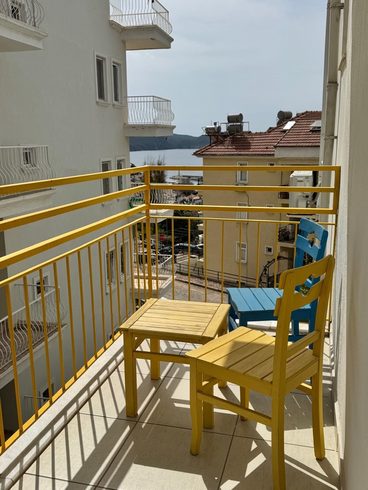 A balcony with yellow railings, a wooden table, and a blue chair.