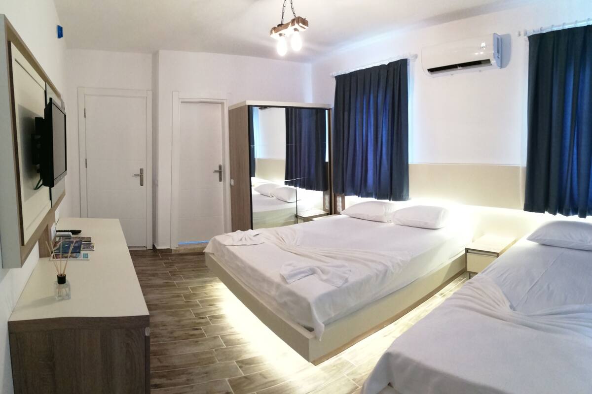 A hotel room with a bed, bedside table, mirror, and a TV on the wall.