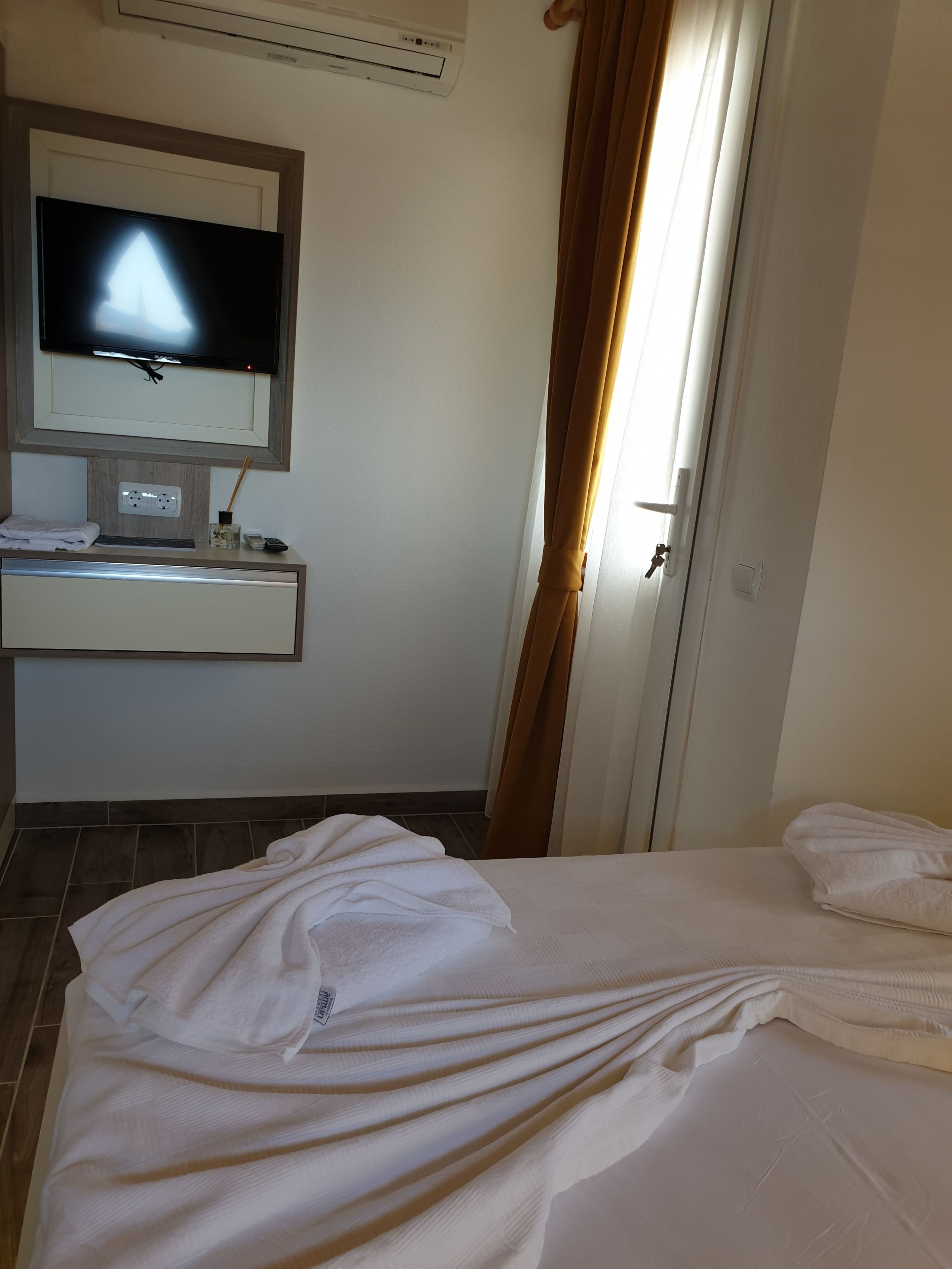 Una camera d'albergo con un letto, una televisione fissata al muro, un comodino con un telecomando e una porta con tende.