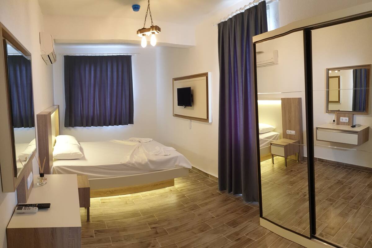 A modern hotel room with a bed, bedside table, mirror, and a large mirror wall.