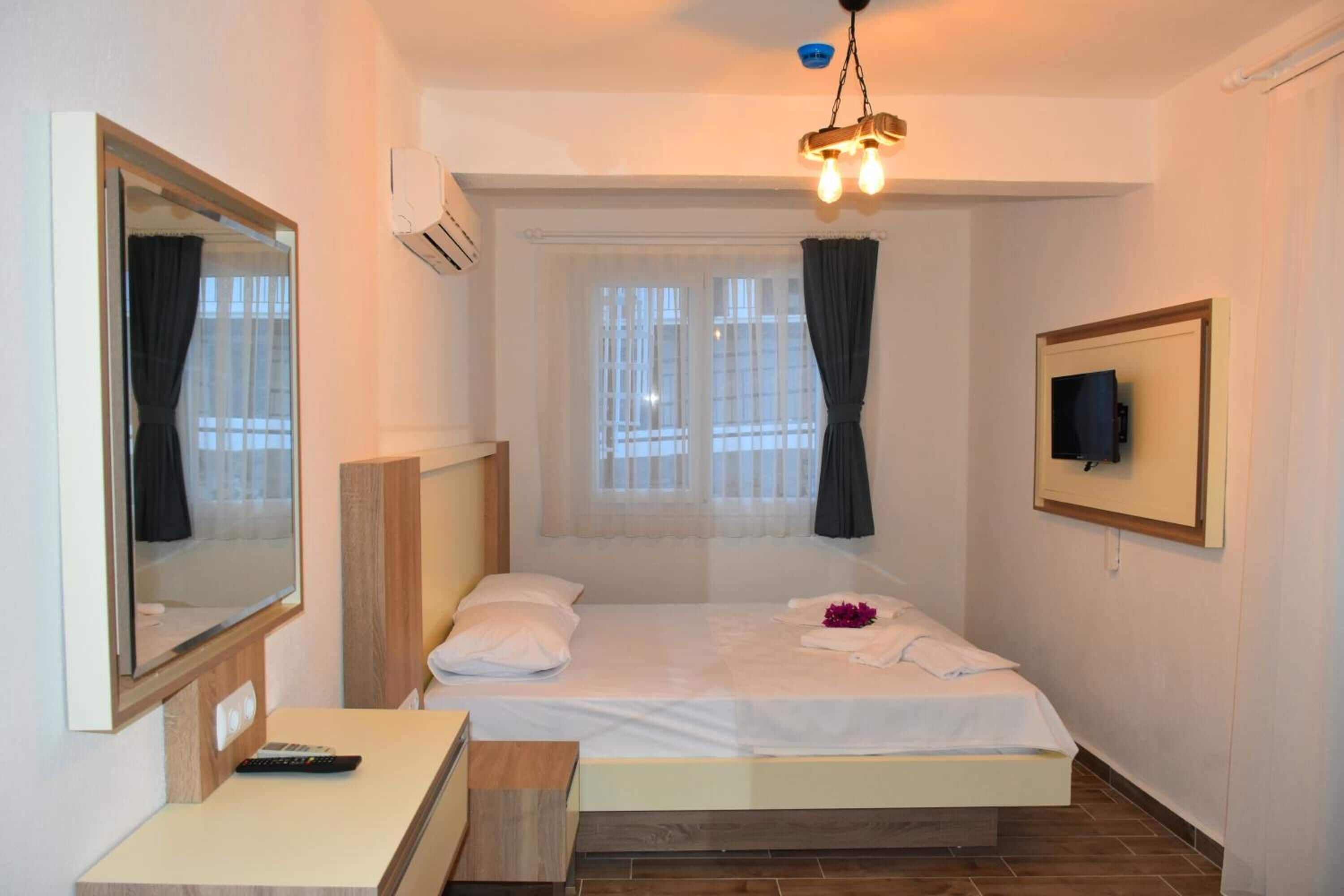 A hotel room with a bed, a desk, a chair, a TV mounted on the wall, and an air conditioning unit.