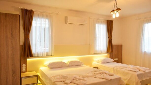A hotel room with two beds, a nightstand, an air conditioning unit, and a hanging light fixture. - Limon Pansiyon (Kas)