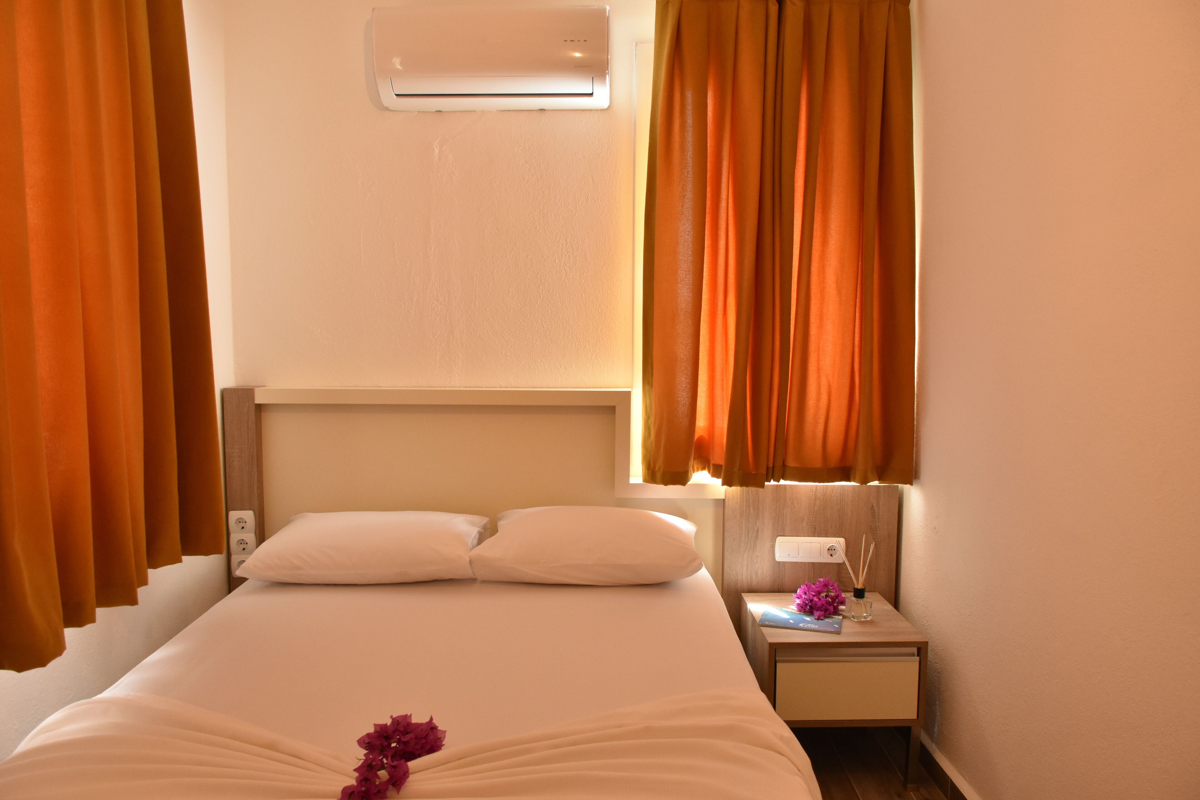 Une chambre d’hôtel avec un lit, un climatiseur, une table de chevet avec une lampe et des rideaux.