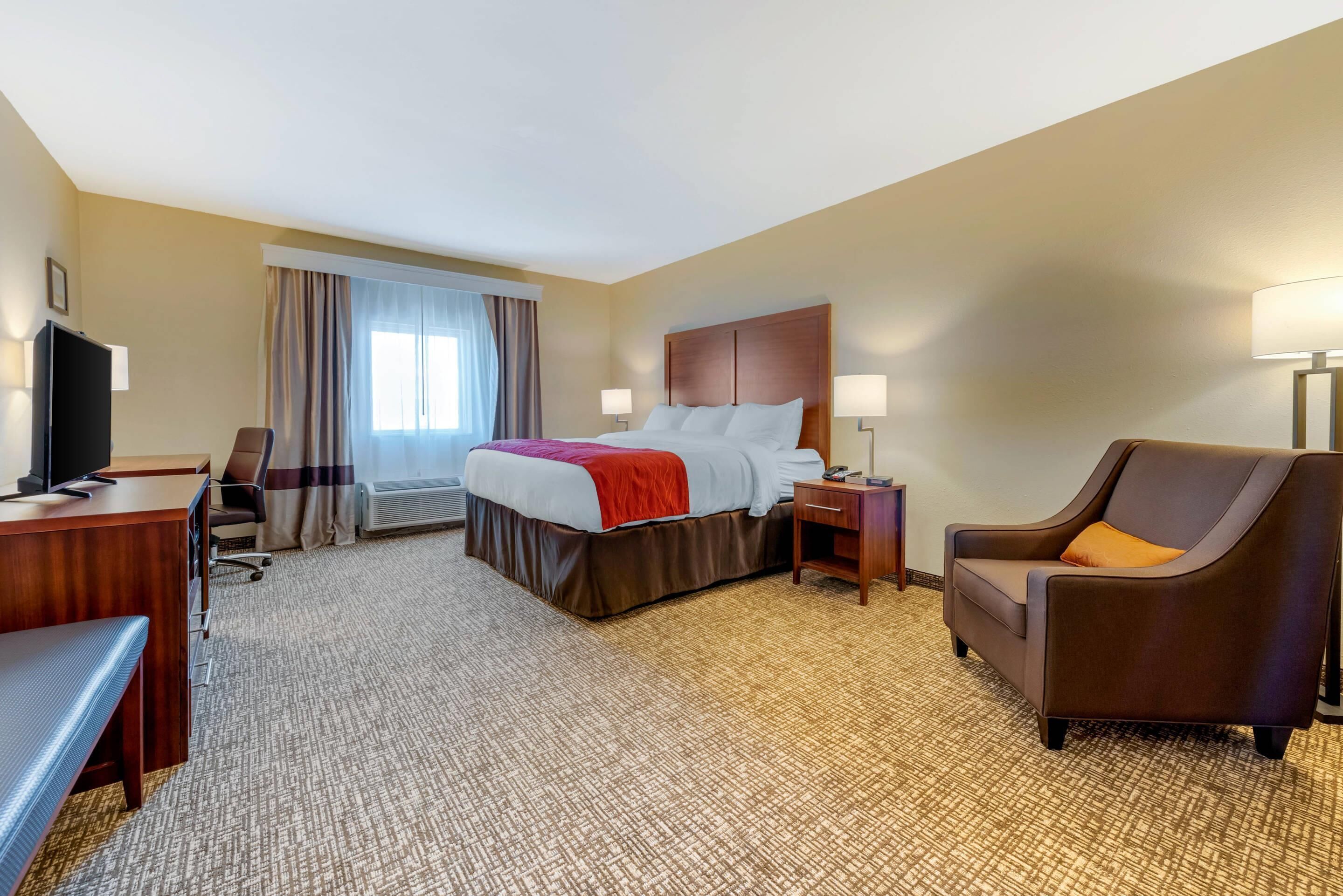Une chambre d’hôtel avec un lit, un bureau, une chaise, une télévision et une lampe.