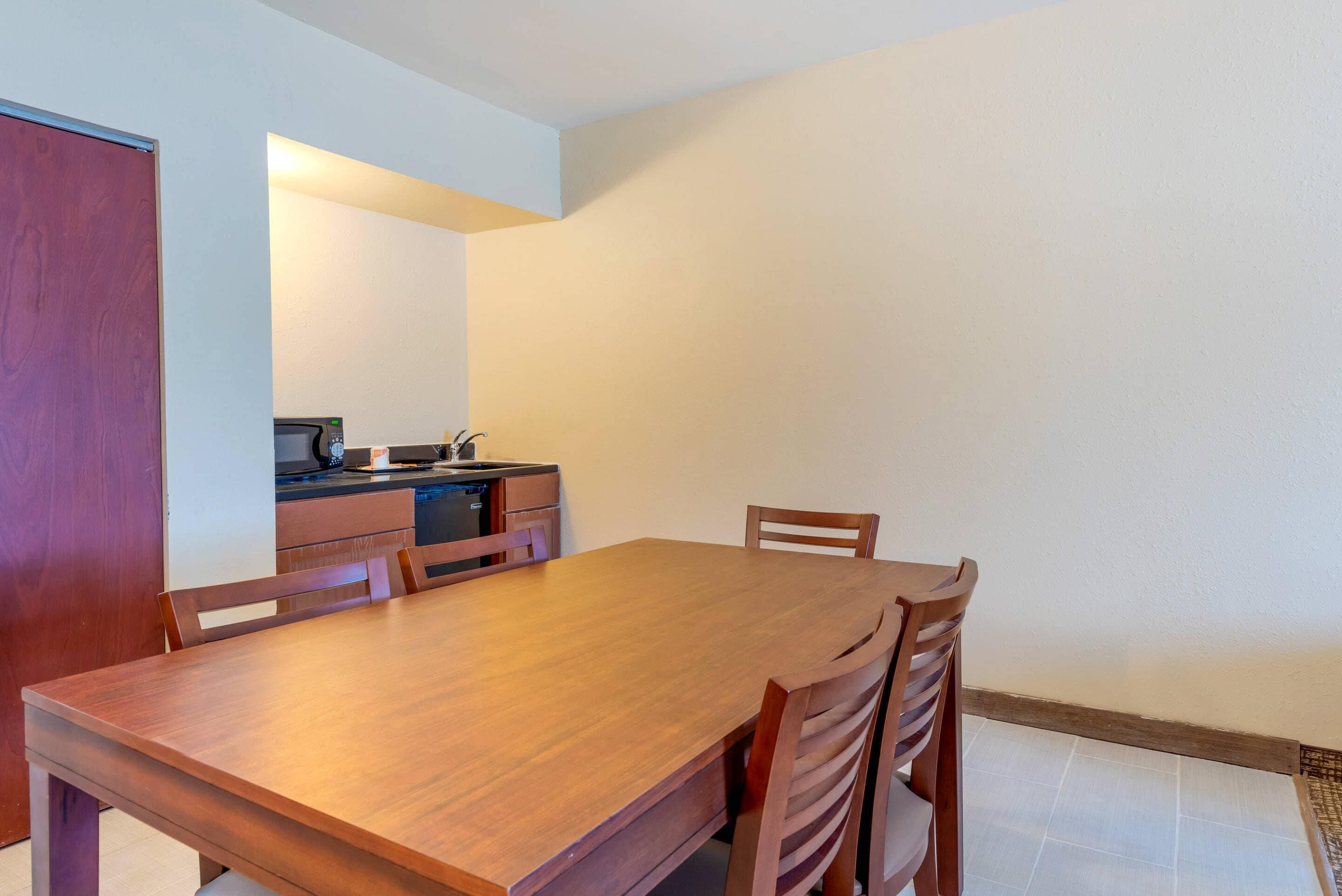Un coin repas avec une table et des chaises en bois, une cuisine en arrière-plan et un mur blanc.