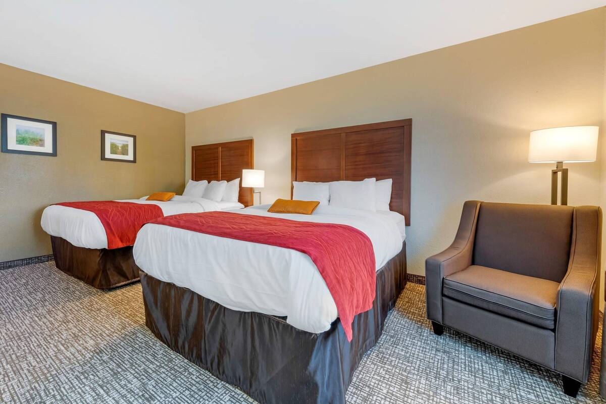 A hotel room with two beds, a chair, and a lamp.