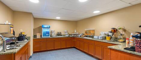 A hotel kitchen with granite countertops, wooden cabinets, and a coffee station.