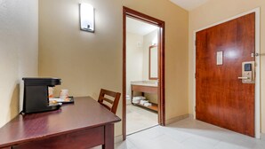 A hotel room with a wooden desk, a coffee machine, a chair, a bathroom with a sink and towels, and a wooden door. - Comfort Inn & Suites Michigan City South (Michigan City)