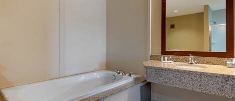 A modern bathroom with a freestanding bathtub, a granite countertop sink, and a large mirror.