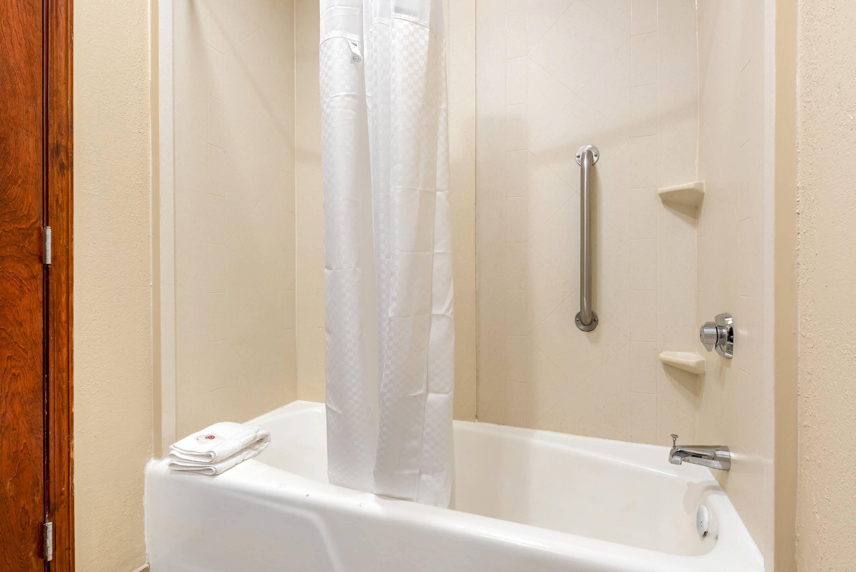 Un bagno con una vasca da bagno bianca, una tenda da doccia, una maniglia di sostegno e un portascopevoli.