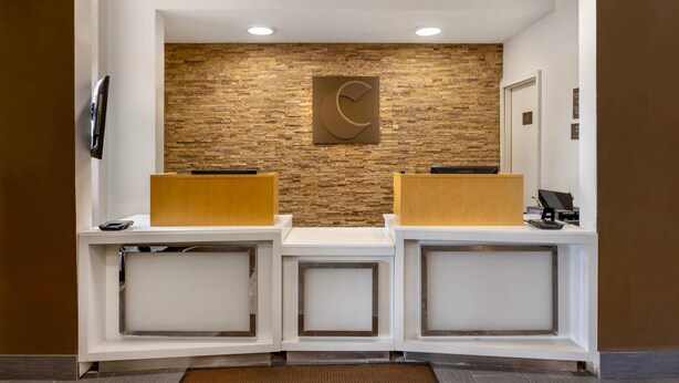 A reception area with a stone wall, a clock, and two reception desks. - Comfort Inn & Suites Michigan City South (Michigan City)