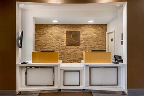 A reception area with a stone wall, a clock, and two reception desks. - Comfort Inn & Suites Michigan City South (Michigan City)
