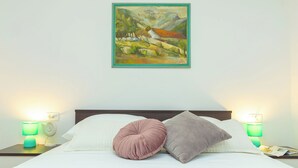 Una cama bien hecha con dos almohadas, un cuadro en la pared y dos lámparas de noche.