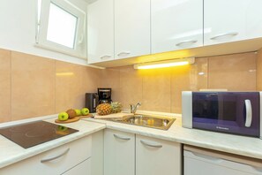 Cozinha moderna com armários brancos, micro-ondas embutido, pia e bancada com frutas e cafeteira.