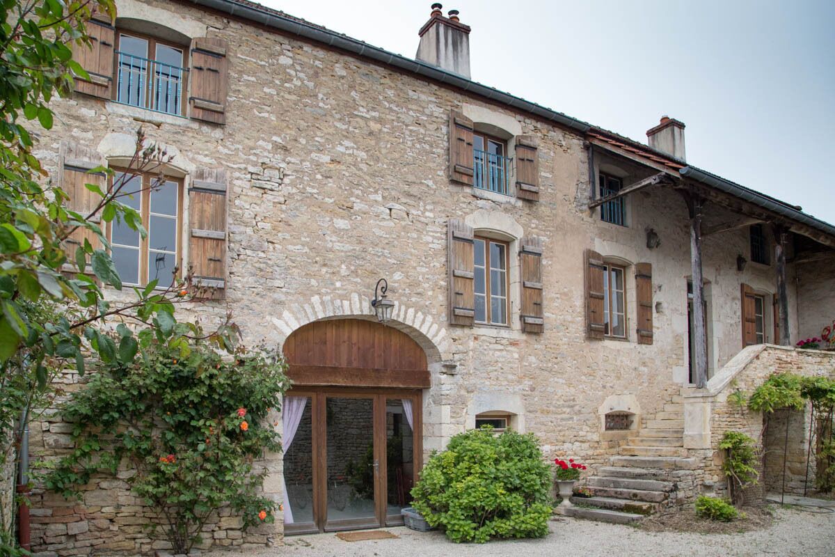 Un edificio de piedra con contraventanas de madera, una entrada central en arco y una pequeña escalera que lleva a una puerta.