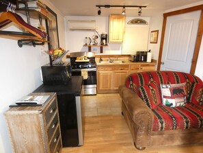 Een kleine keuken met een fornuis, oven en spoelbak, een houten eettafel en een bank met een decoratief plaid.