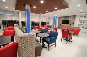 A modern indoor seating area with red and blue chairs, wooden tables, and a patterned bench.