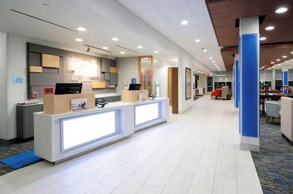 A modern hotel reception area with a reception desk, check-in counter, and a waiting area with chairs and tables.