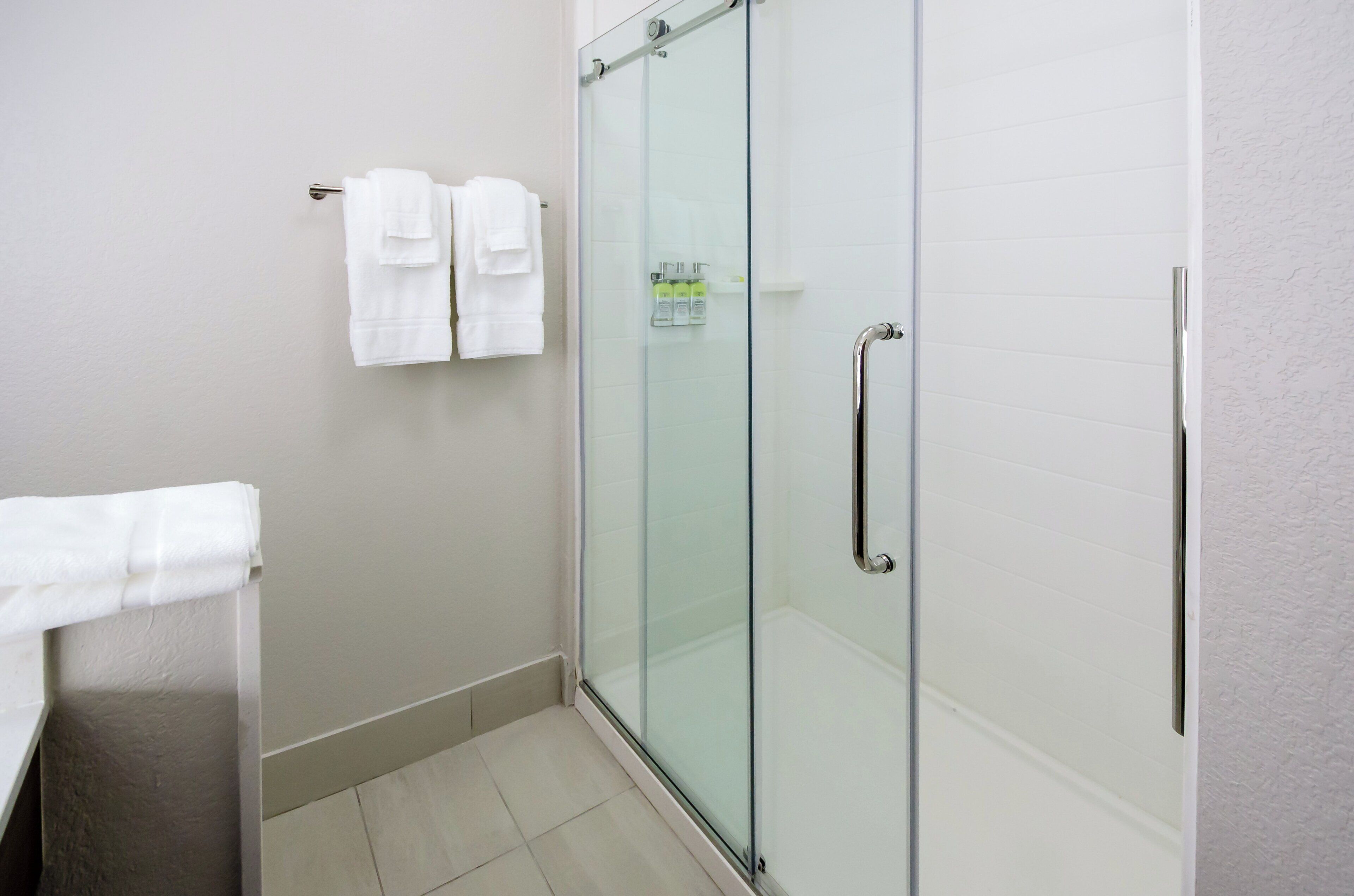 A modern bathroom with a glass shower enclosure, a towel rack with two towels, and a small shelf with toiletries.