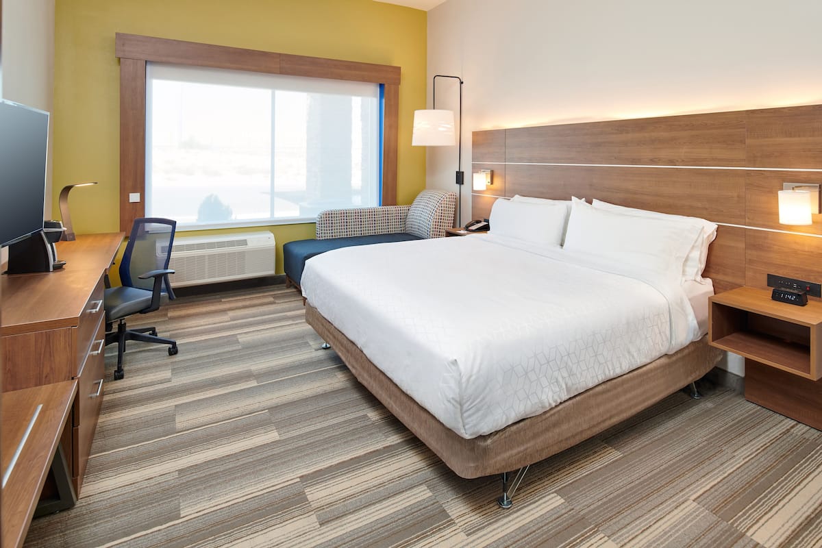 A hotel room with a large bed, a desk with a computer, a chair, and a window with a view.