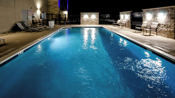 A swimming pool with lounge chairs and stone walls, surrounded by a low fence. - Holiday Inn Express & Suites Taylor by IHG (Taylor)