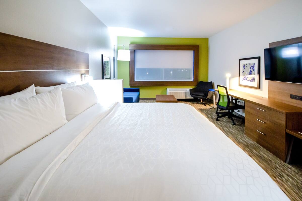 A hotel room with a large bed, a desk with a chair, a television, and a window with a view.
