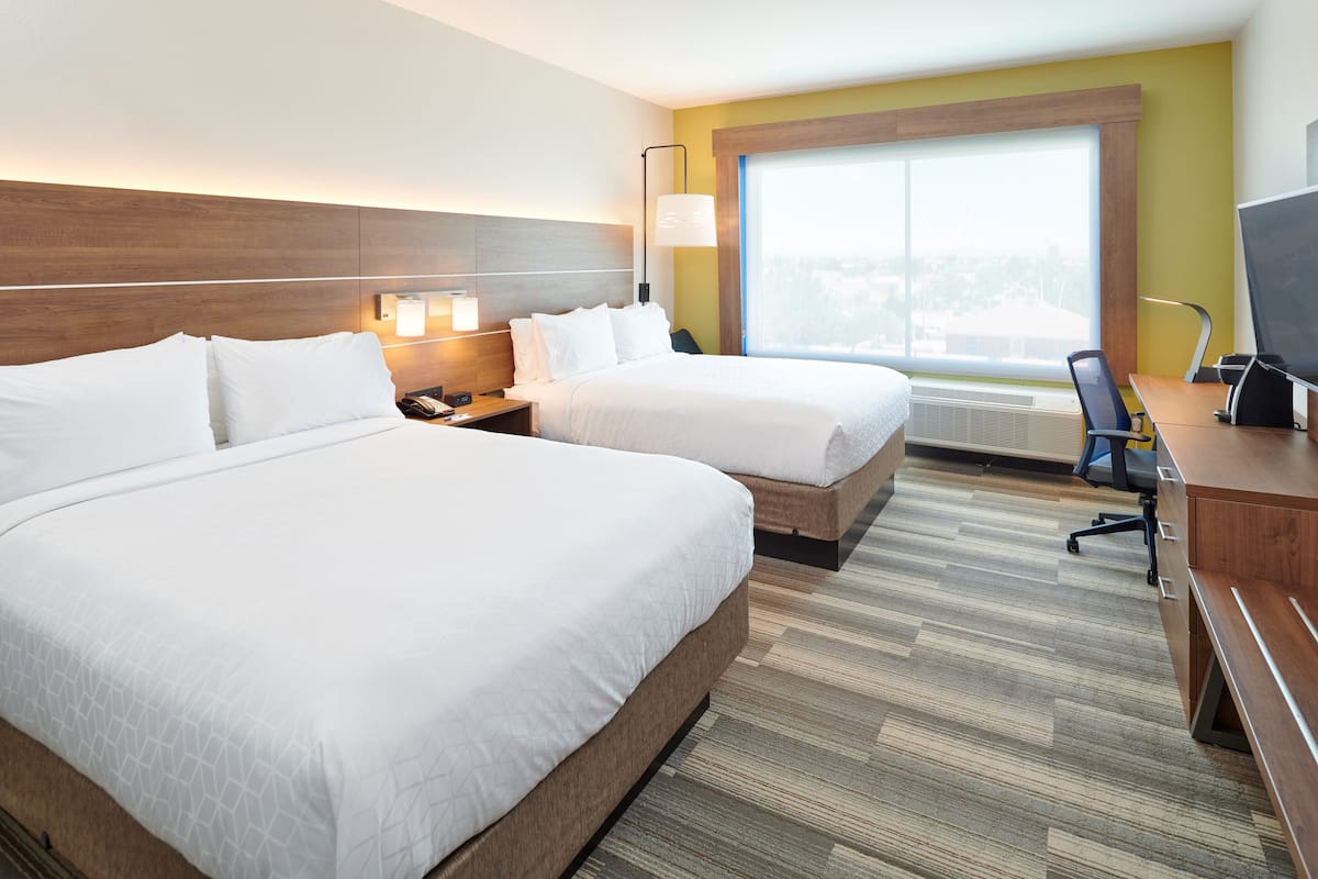 A hotel room with two beds, a desk, a chair, a television, and a large window.