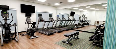 A gym with multiple treadmills and exercise bikes, a wooden floor, and a large mirror wall.