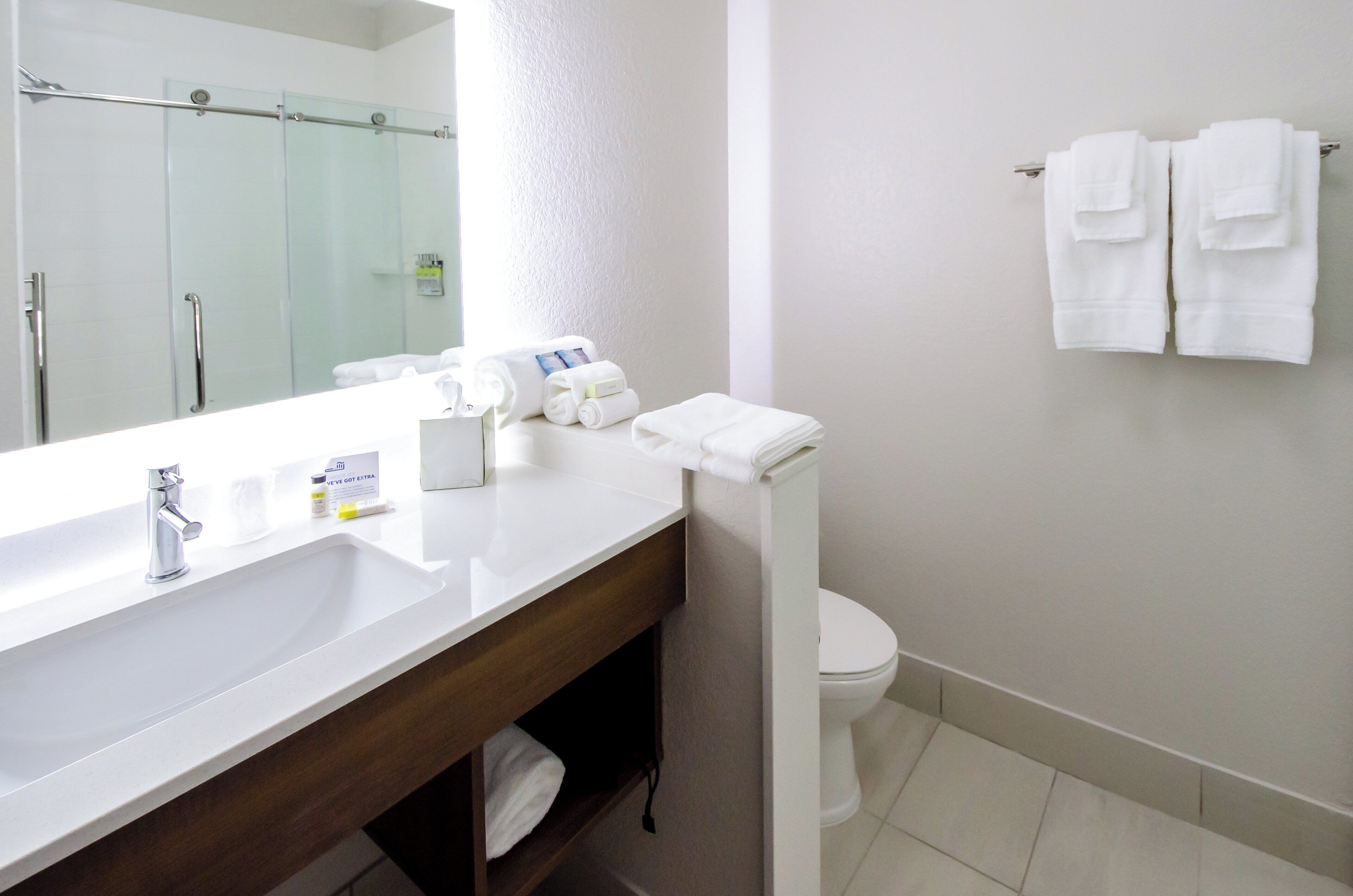 A hotel bathroom with a white sink, a mirror, a toilet, and a towel rack with towels.