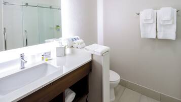 A hotel bathroom with a white sink, a mirror, a toilet, and a towel rack with towels.