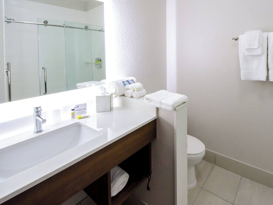 A hotel bathroom with a white sink, a mirror, a toilet, and a towel rack with towels.