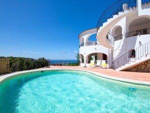 Uma villa moderna com uma piscina grande, várias varandas e vista para o mar.