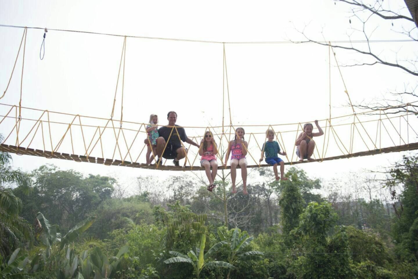 A group of people sitting on a rope bridge in a natural setting.