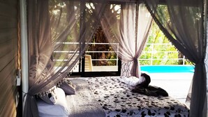 A bed with a canopy, a view of a swimming pool, and a window with a view of greenery. - Relaxing Luxury Jungle Escape in Quepos with Jacuzzi, Zipline, Pool and more (Parrita)